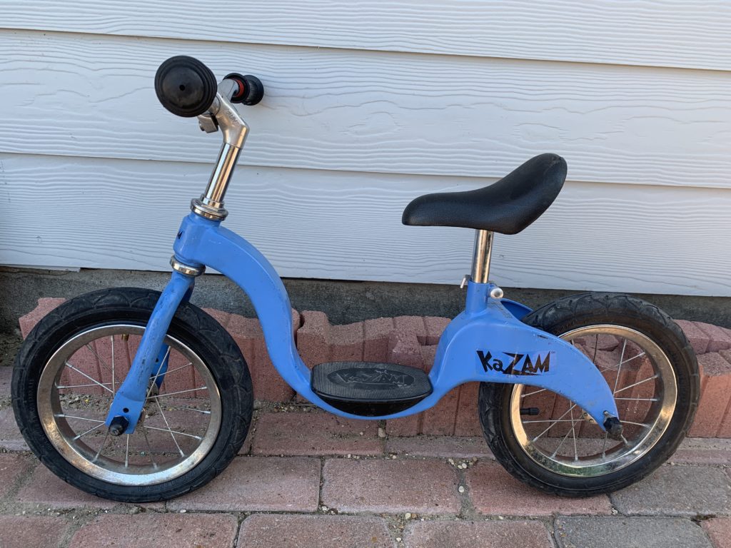 Small light blue bicycle with 12" diameter wheels with no pedals on a brick walk